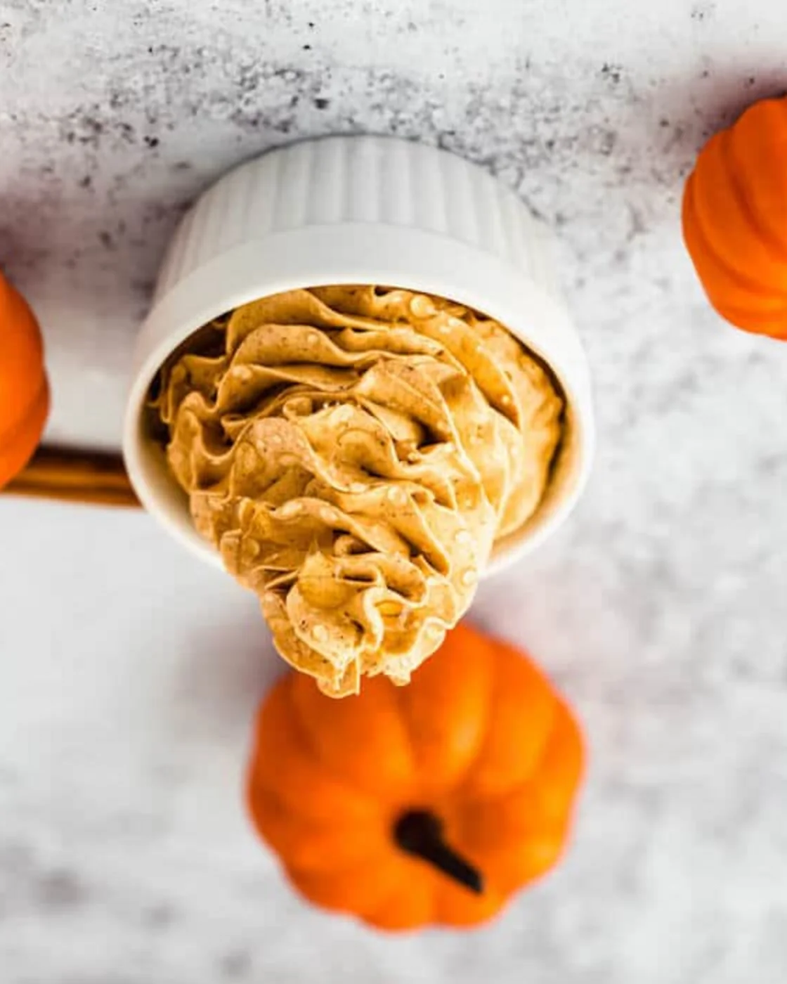 Creamy, fluffy pumpkin spice honey butter served in a cup with pumpkins nearby.