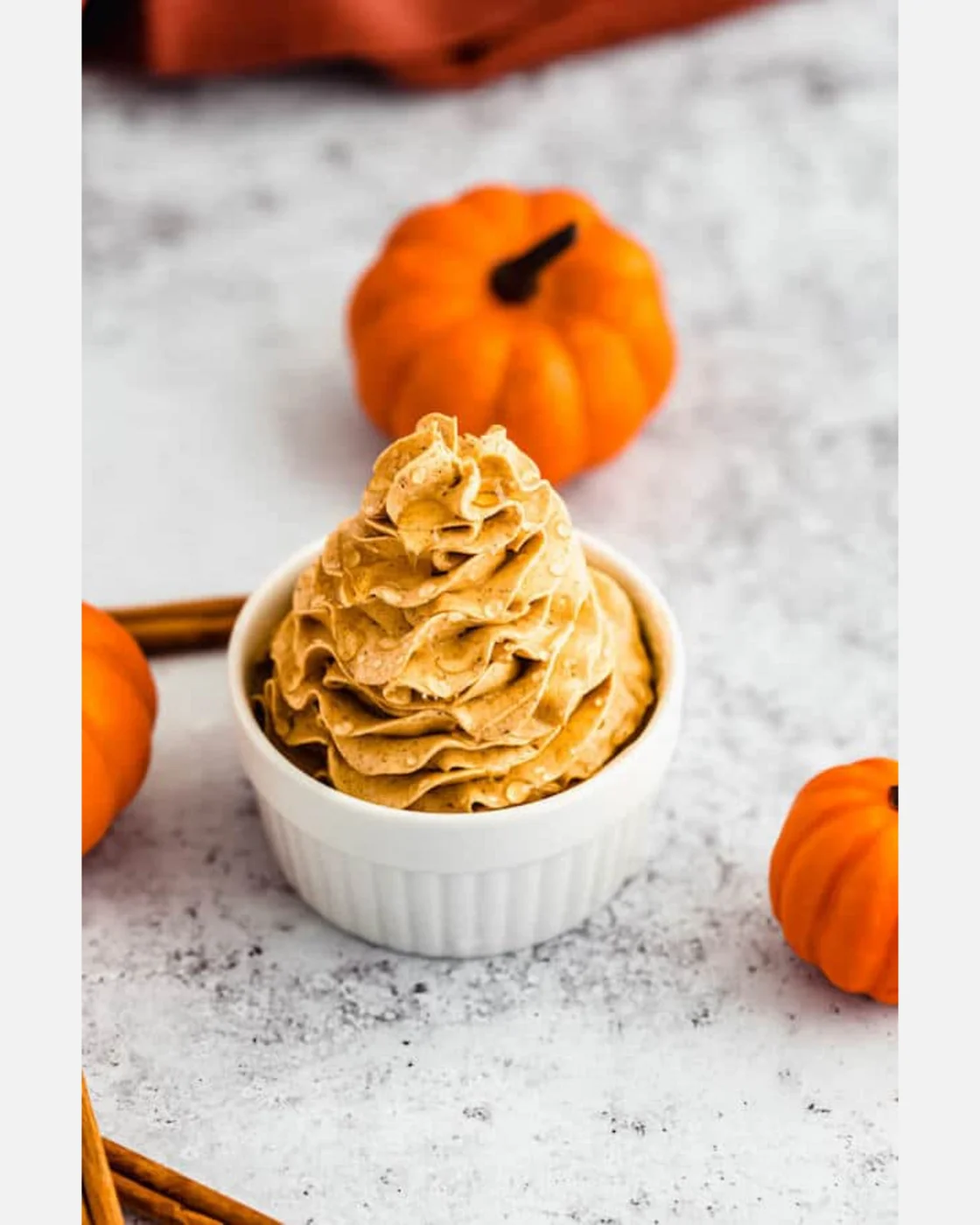 Creamy whipped pumpkin spice honey butter with pumpkins on a white surface.