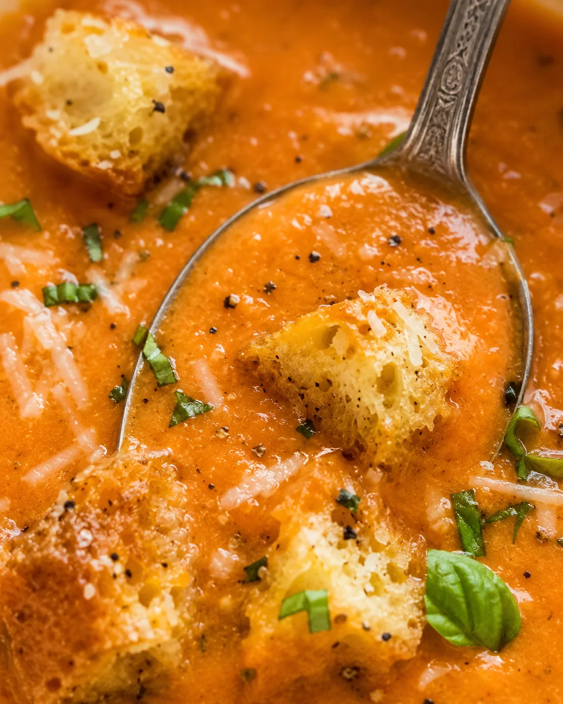 Close-up detail of creamy tomato basil soup with crouton, grated cheese, and chopped basil